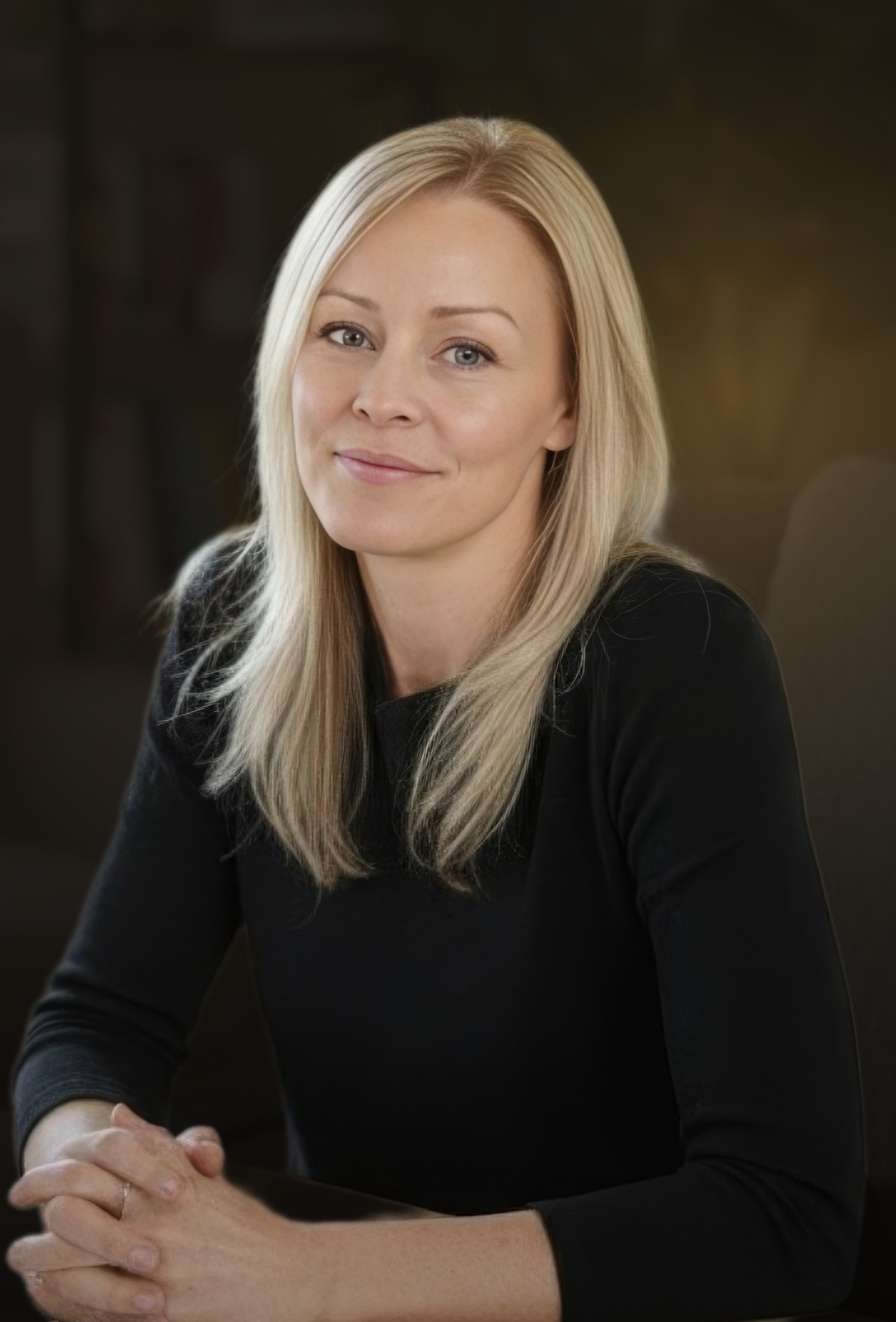 Dominique Poulin, assise, mains jointes, sourire calme — portrait sur fond sombre